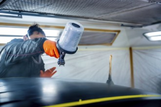 Automotive technician wearing safety gloves and mask meticulously applying a fresh coat of paint to
