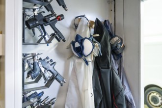 Organized racks of professional spray guns, respirators and protective suits in an automotive paint