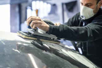 Professional mechanic performing essential work in a car body and paint shop, sanding the vehicle's