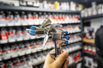 Hand holding a high pressure spray gun, selecting paint colors from shelves in an automotive
