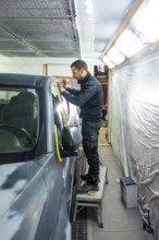 Mechanic applying masking tape meticulously on a car body before painting in a professional