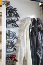 Modern spray guns and protective gear, including a disposable suit and a respirator mask, hanging