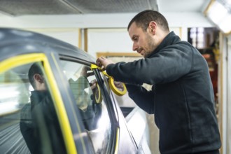 Automotive technician carefully applying yellow masking tape around a car window and trim before a