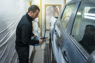 Worker preparing car body for painting in an automotive repair facility, applying solution to the