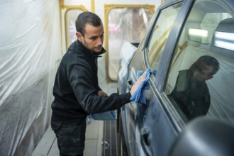 Man carefully wiping car body panels with a blue microfiber cloth inside a professional spray