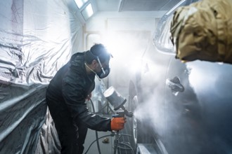 Professional automotive technician applying a fresh coat of paint to a vehicle in a specialized