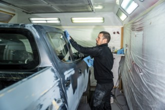 Auto body technician carefully cleaning and preparing a pickup truck in a professional paint booth,