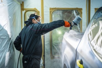 Auto body painter wearing protective equipment and holding a spray gun, expertly applying a fresh