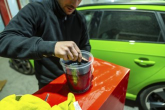 Male worker preparing automotive paint in a plastic container with a lime green vehicle visible in