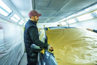 Skilled technician carefully masking vehicle with brown paper and tape, preparing it for a