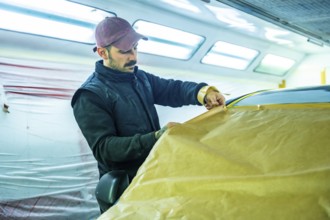 Auto body technician carefully applying masking paper and tape to a vehicle in a professional car