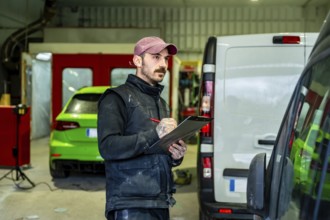 Auto body shop technician checking details on a white van and a green car in the background,