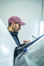 Auto technician wearing a cap writing details on a clipboard while inspecting vehicle condition in