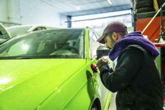 Auto body technician working on a vibrant green car, using a polisher to refine and enhance the
