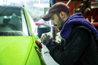 Man polishing a bright lime green car with a buffer in an auto body shop, applying a fine finish