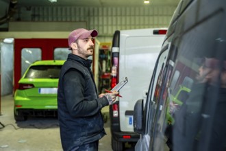 Mechanic holding a clipboard and pen while inspecting a commercial van in a car body and paint
