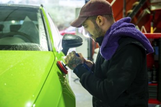 Mechanic meticulously polishing a vibrant green car body with a rotary polisher, improving its