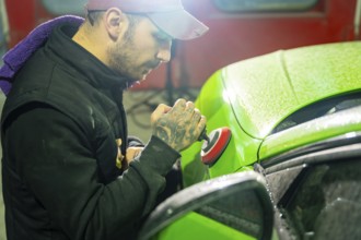 Automotive technician buffs vibrant green car paint with a professional orbital polisher in a