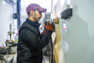Auto body technician sanding a car panel in a repair shop, preparing the surface for painting