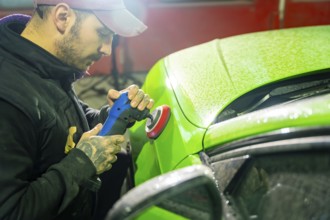 Professional automotive technician using an orbital buffer to polish a glossy green car body in a
