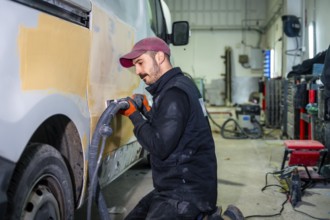 Auto body technician working on a van, utilizing a power sander with vacuum attachment to smooth