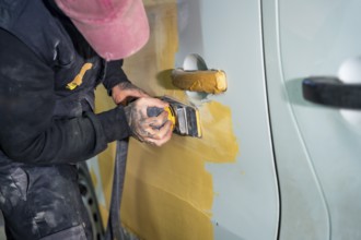 Auto body technician sanding a car door to prepare its surface for painting after repairs,