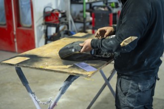 Mechanic preparing a car part by carefully sanding the surface on a workbench, ensuring a smooth