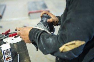 Auto body technician preparing a car surface for painting using an orbital sander, demonstrating