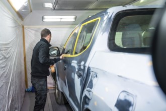 Mechanic applying masking tape to a car surface, meticulously preparing the vehicle for a fresh