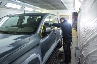 Automotive technician preparing a vehicle for painting by carefully applying protective masking
