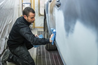 Auto body technician in a workshop cleaning and preparing a car door for painting with a microfibre