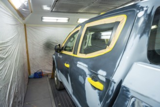 Vehicle in a body shop prepped for painting, masked with tape over windows and trim, primed and