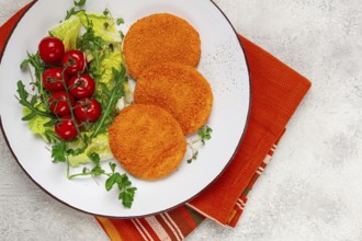 Crispy fried fish cutlets, fish burgers, on a white plate, with fresh lettuce leaves, arugula and