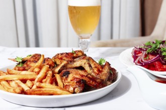 Delicious barbecue chicken wings, with French fries, salad and a refreshing drink, at a cozy table,