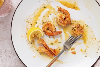 The remains of fried shrimp in oil with spices, on a white plate, with a fork, there are no people
