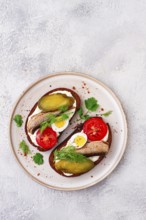 Sandwiches on rye bread, with sprats, quail eggs, fresh tomatoes and pickled cucumber, appetizer,