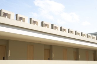 A row of air conditioning units on a modern building rooftop against a clear blue sky in Thailand.