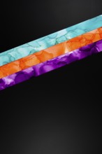 Vibrant diagonal colors inks stripes of teal, orange, and purple on a dark background. This