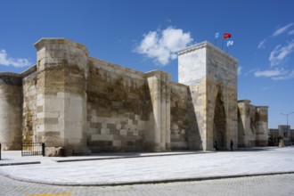 Impressive stone wall with high gate under blue sky with waving flags, Sultanhani caravanserai, on