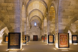 Large stone hall with illuminated carpets between imposing arches, Sultanhani caravanserai, on the