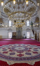 Magnificent interior of a mosque with a large chandelier and richly decorated carpet, illuminated