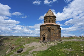 Old church on a hill under blue sky with clouds surrounded by grass and ruins, Armenian Church of