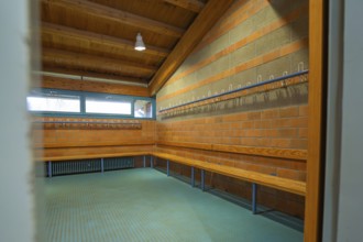 A changing room with long wooden benches and brick walls, hooks for clothes, blue light,
