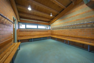 Spacious changing room with wooden ceiling and brick walls as well as benches and bright lamps,