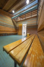 A light-flooded changing room with wooden benches and brick walls, turquoise floor, Schlehengäu