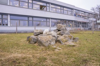 Piles of stones on the lawn in front of a school building with scaffolding in the background,