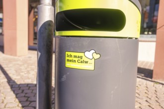A trash can with city cleanliness sticker on a sunny day in public spaces, Calw, Calw district,