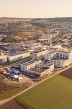 Aerial view of an industrial plant with modern buildings and surrounding fields in warm sunlight,