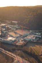 View of an industrial landscape with construction crane and buildings at the foot of wooded hills