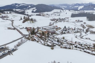 Wintery mountain village surrounded by snow-covered roads and mountains taken from the air,